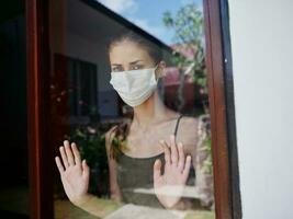 maskiert Frau suchen aus das Fenster traurig aussehen Quarantäne foto