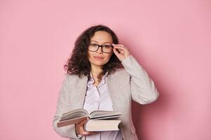 zuversichtlich reifen Frau, Schule Lehrer, Professor, Erzieher, Geschäft Trainer im stilvoll Brille, halten Buch im Hände foto