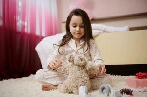 glücklich wenig Kind Mädchen spielen mit ein Plüsch Spielzeug im ihr Zimmer. International Kinder- Tag und sorglos Kindheit Konzept foto