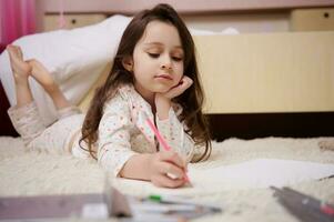 kaukasisch süß Baby Mädchen im stilvoll Pyjama, Zeichnung Bild mit bunt Bleistifte drinnen foto