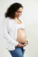heiter ethnisch schwanger Frau 30er Jahre alt, erwarten ein Baby, berühren Bauch auf Weiß Hintergrund. Schwangerschaft 6 Monat. 24 Wochen. foto