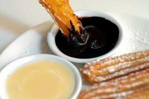 warm Spanisch Churros Krapfen Eintauchen zu dunkel Schokolade Soße foto