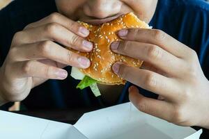 Burger im ein Jungs Hand, ein hungrig Junge hält ein Cheeseburger Vor Essen Es, Kopieren Raum foto