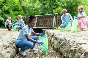 Freiwillige afrikanisch Frau Sammeln Plastik Müll auf Küste von das Fluss. Reinigung Umgebung Konzept foto