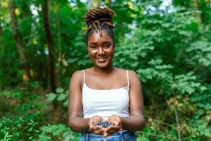 afrikanisch Frau mit Hand voll von frisch gepflückt organisch Blaubeeren foto