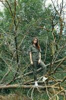 Frau im Turnschuhe auf ein gebrochen Baum im das Wald und ein Grün Overall foto