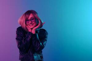 genossen glücklich blond Frau im Leder Jacke prickelnd Kleid modisch Sonnenbrille zurücklehnen auf Hände posieren isoliert im Blau Rosa Farbe Licht Studio Hintergrund. Neon- Party Cyberpunk Konzept. Kopieren Raum foto