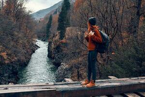 Frau steht auf ein Brücke Über ein Fluss im das Berge Herbst Wald Reise foto