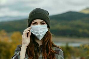 Frauen im medizinisch Maske Berg Porträt im das Herbst Natur Hintergrund foto