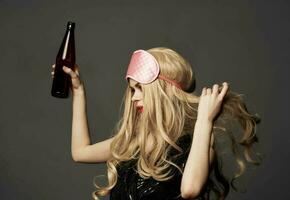 wütend Frau mit ein Flasche von Bier im ihr Hand mit hell bilden und ein Rosa Schlaf Maske foto