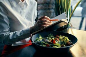 Notizblock mit ein Stift im Hand und Salat im ein Teller Restaurant Cafe Inschrift foto