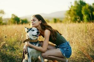 Frau lächelnd und umarmen ihr Hund Sitzung im ein Feld mit ein Dackel Hund lächelnd während Ausgaben Zeit draußen mit ein Freund Hund im Herbst beim Sonnenuntergang während Reisen foto