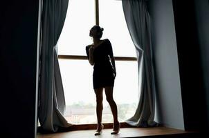 Frau in der Nähe von das Fenster im schwarz Kleid und posieren foto