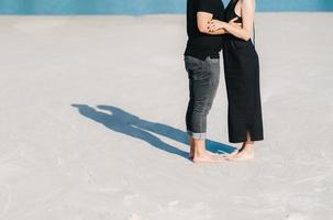 junges Paar ein Mann mit einem Mädchen in schwarzen Kleidern geht auf dem weißen Sand