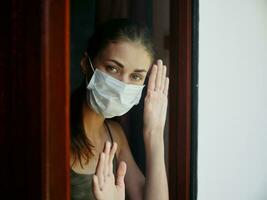 Frau im medizinisch Maske suchen aus das Fenster Nahansicht foto