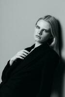 Porträt von ein schön blond im ein klassisch Jacke gelehnt gegen das Mauer im das Studio. schwarz und Weiß Stil. Konzept zum Kleidung Marken foto