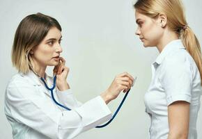 Arzt mit ein Stethoskop untersucht ein Frau im ein Weiß T-Shirt auf ein Licht Hintergrund foto