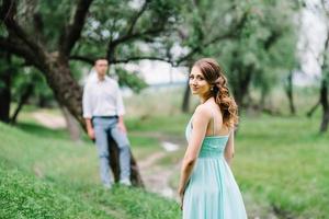 Ein glücklicher Kerl in einem weißen Hemd und ein Mädchen in einem türkisfarbenen Kleid gehen im Waldpark spazieren foto