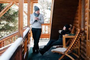 ein paar junge Leute, ein Mann und ein Mädchen auf der Veranda eines schneebedeckten Holzhauses foto