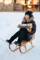 Mädchen sitzt in einem Schlitten lächelnd und hält Holz in ihren Händen foto