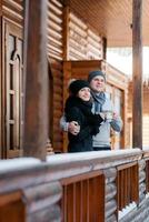 ein paar junge Leute, ein Mann und ein Mädchen auf der Veranda eines schneebedeckten Holzhauses foto