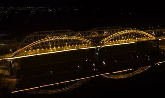 hell Beleuchtung, Brücken mit Bögen, Nacht Stadt. ein Straße Brücke über das Fluss, genommen von ein Drohne. foto