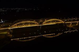 hell Beleuchtung, Brücken mit Bögen, Nacht Stadt. ein Straße Brücke über das Fluss, genommen von ein Drohne. foto