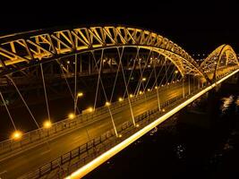 hell Beleuchtung, Brücken mit Bögen, Nacht Stadt. ein Straße Brücke über das Fluss, genommen von ein Drohne. foto