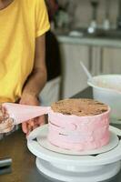 Frau Spreads Rosa Sahne auf Kuchen mit Gebäck Tasche, Nahansicht. Kuchen Herstellung Verfahren, selektiv Fokus foto