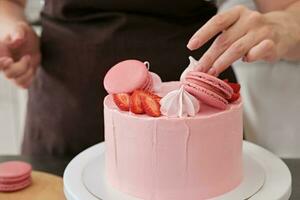 Frau Gebäck Koch dekoriert Rosa Kuchen mit Makronen und Beeren, Nahansicht. Kuchen Herstellung Verfahren, selektiv Fokus foto