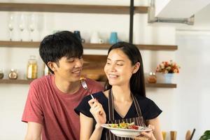 Ein junges asiatisches Paar isst zusammen und lächelt glücklich, während es seinen Salat in der Küche kocht. foto