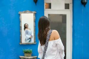 schön Frau auf Weiß Kleid suchen beim Sie selber auf ein Spiegel auf das bunt Straßen von das kolonial ummauert Stadt von Cartagena de Indien foto