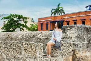 schön Frau auf Weiß Kleid Sitzung allein beim das Wände Umgebung das kolonial Stadt von Cartagena de Indien foto