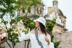 schön jung Frau versuchen auf Hüte zu Kaufen einer von ein Straße Verkäufer im Cartagena de Indien ummauert Stadt foto