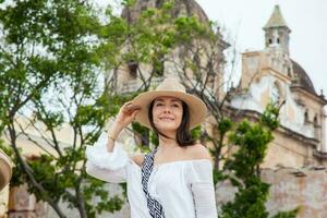 schön jung Frau versuchen auf Hüte zu Kaufen einer von ein Straße Verkäufer im Cartagena de Indien ummauert Stadt foto