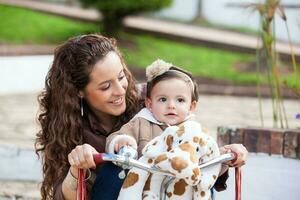 schön jung Mutter spielen mit ihr einer Jahr alt Baby draußen. mit Mama Reiten meine Dreirad foto