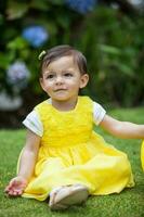 Süss einer Jahr alt Baby Mädchen gekleidet im Gelb Bewässerung das Pflanzen beim das Garten foto