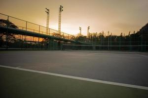 selektiver Fokus der Grundlinie eines Tennisplatzes mit einem Sonnenuntergangshimmelhintergrund. Landschaft des Sportplatzes. foto