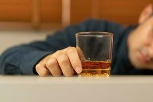 Alkoholismus, deprimiert asiatisch jung Mann Schlaf auf Tabelle während Trinken alkoholisch Getränk, halten Glas von Whiskey allein beim Nacht. Behandlung von Alkohol Sucht, leiden Missbrauch Problem Alkoholismus Konzept foto