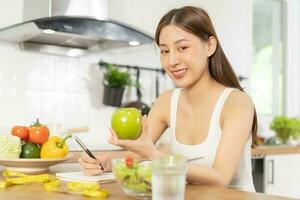 Diät, Diät asiatisch jung Frau Arbeiten, schreiben Diät planen richtig Ernährung, halt Grün Apfel, Gemüse Salat ist Essen zum gut Gesundheit nicht wählen Essen Müll Lebensmittel. Ernährungsberater weiblich, Gewicht Verlust Person. foto