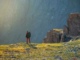Fotograf mit ein groß Rucksack nimmt Bilder von ein schön Berg Landschaft auf das Kante von ein Cliff. foto