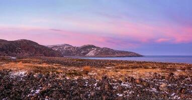 tolle Sonnenaufgang Polar- Landschaft mit ein Weiß Schnee Grat von Berge hinter das felsig Berge und ein Cliff. wunderbar Berg Landschaft mit Tundra auf das Barents Meer. foto