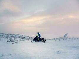 männlich auf Schneemobil im das Abend Polar- hügel. allein Mann Reiten oben ein Hügel auf Schneemobil. extrem Winter Sport, Polar- aktiv Urlaube im das hart Nord Natur. foto