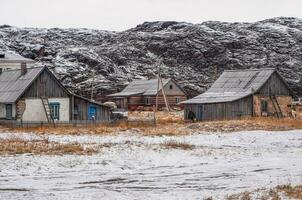 Jahrgang Häuser auf das Hintergrund von schneebedeckt Arktis Hügel. alt authentisch Dorf von Teriberka. Kola Halbinsel. foto