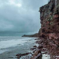 ein Felsen Cliff über das Wasser mit ein Gezeiten Küstenlinie. Weiß Meer foto