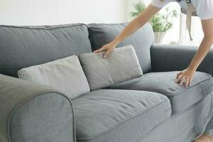 Frau Reinigung und arrangieren Sofa Kissen beim heim. foto