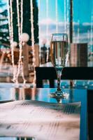 ein Glas von Champagner im das Tabelle gegen das Hintergrund von das Bokeh von ein Nacht Restaurant. Nachtclub, Feier, Weihnachten. foto