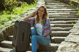 jung Tourist Frau Sitzung durch das Treppe mit ein Koffer foto
