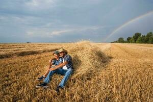 Vater und Sohn sind Stehen im ihr Weizen Feld nach ein erfolgreich Ernte. foto
