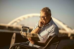 Senior Mann lesen ein Karte draußen mit ein Koffer. Tourist Konzept foto